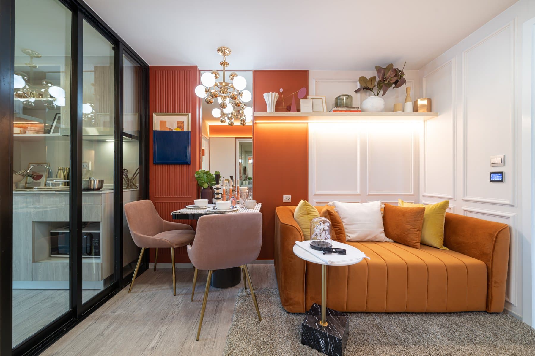 Dining corner of a furnished show unit at Atmoz Portrait Srisaman, with blush upholstered chairs, a brass chandelier and a glazed partition to the kitchen