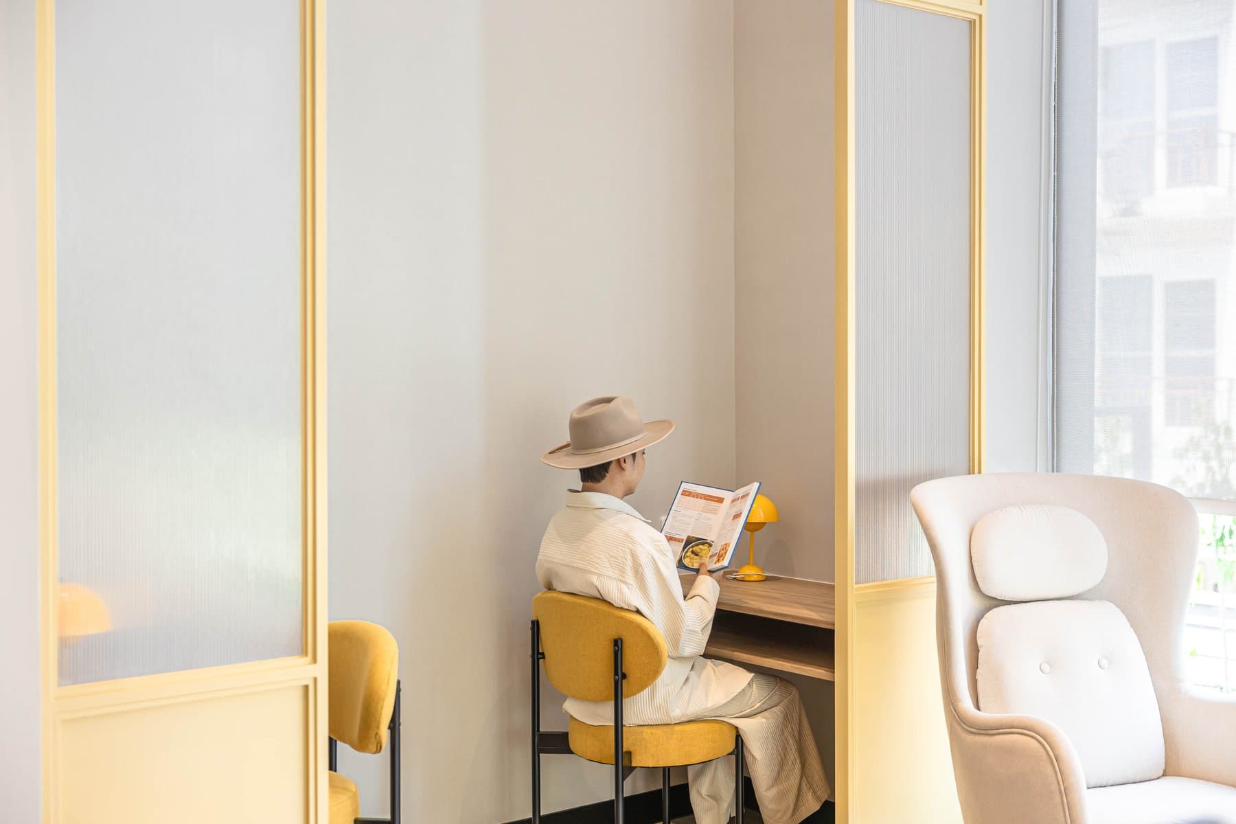 Quiet reading nook at Kave COCO Bangsaen with a pair of cream armchairs and a mustard side chair beside a full-height window
