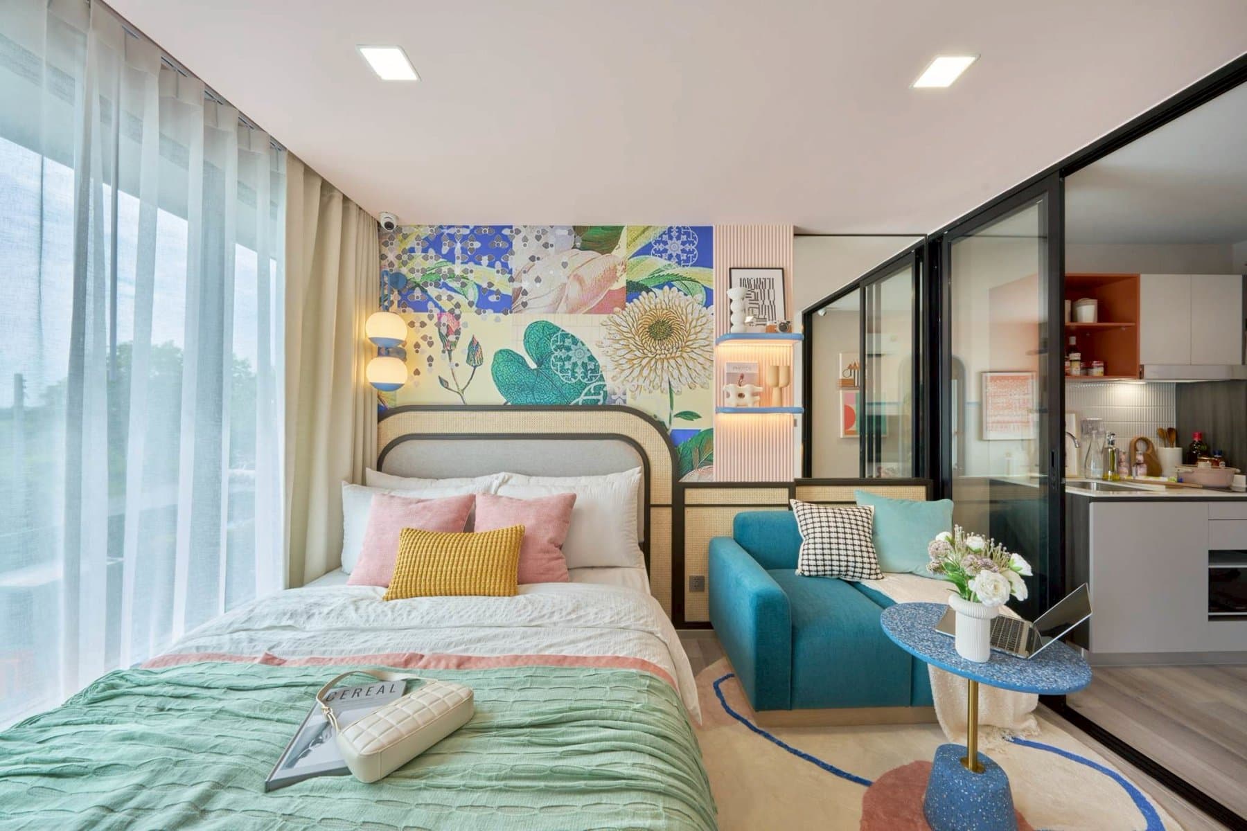 Bedroom of the One Bedroom show unit at Kave Genesis, with a mint-green bed throw, a teal armchair and a round side table beside the glazed partition