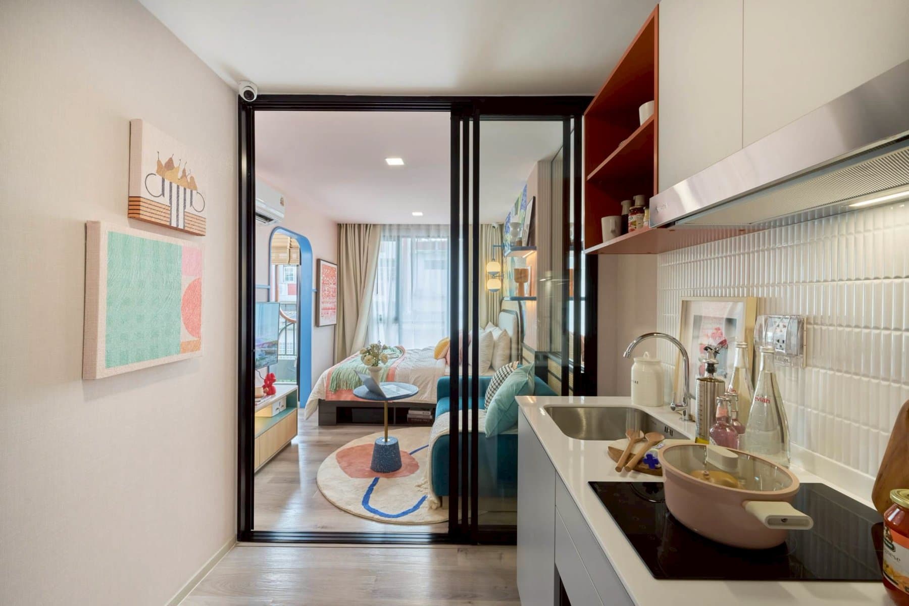 One Bedroom show unit at Kave Genesis Nakhon Pathom seen from the entrance, looking past the white kitchen counter and a black-framed glazed partition to the bedroom and its full-height window