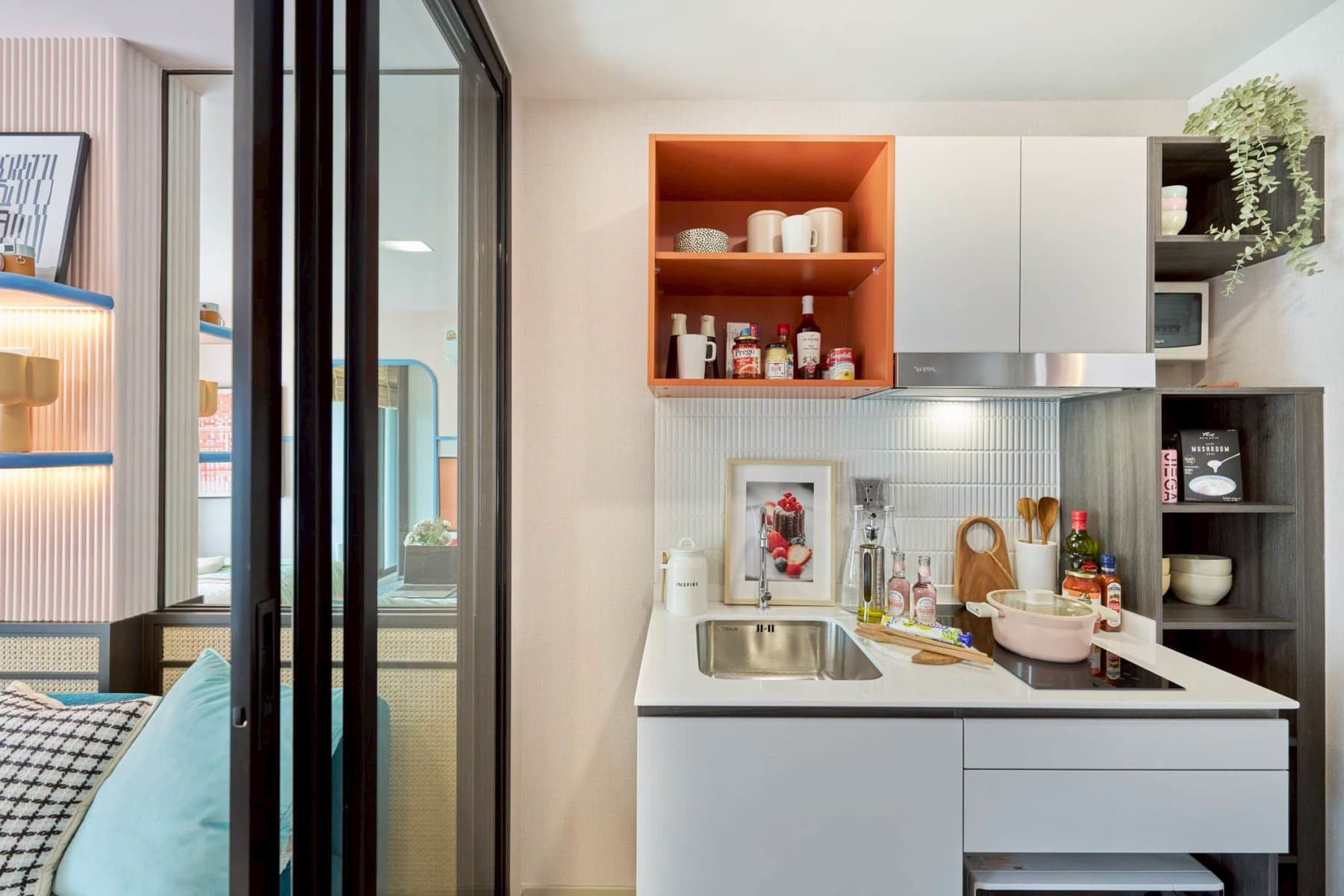 Kitchen at Kave Genesis seen from the bedroom through the black-framed glazed partition, with the hob, sink and open shelving on the far wall