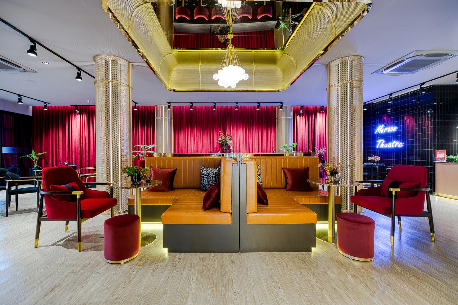 Sales gallery lounge at Maroon Ratchada 32 with red velvet drapery, brass mesh columns, tan leather banquette seating and a gold mirrored ceiling recess.