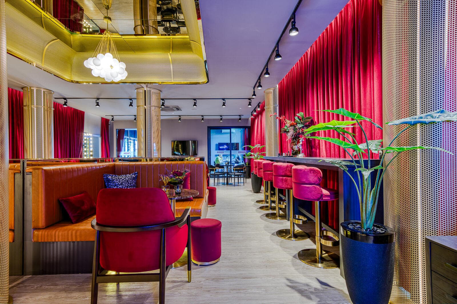 Bar counter and banquette seating inside the Maroon Ratchada 32 sales gallery, with magenta velvet stools, brass screen partition and theatre-style red curtains.