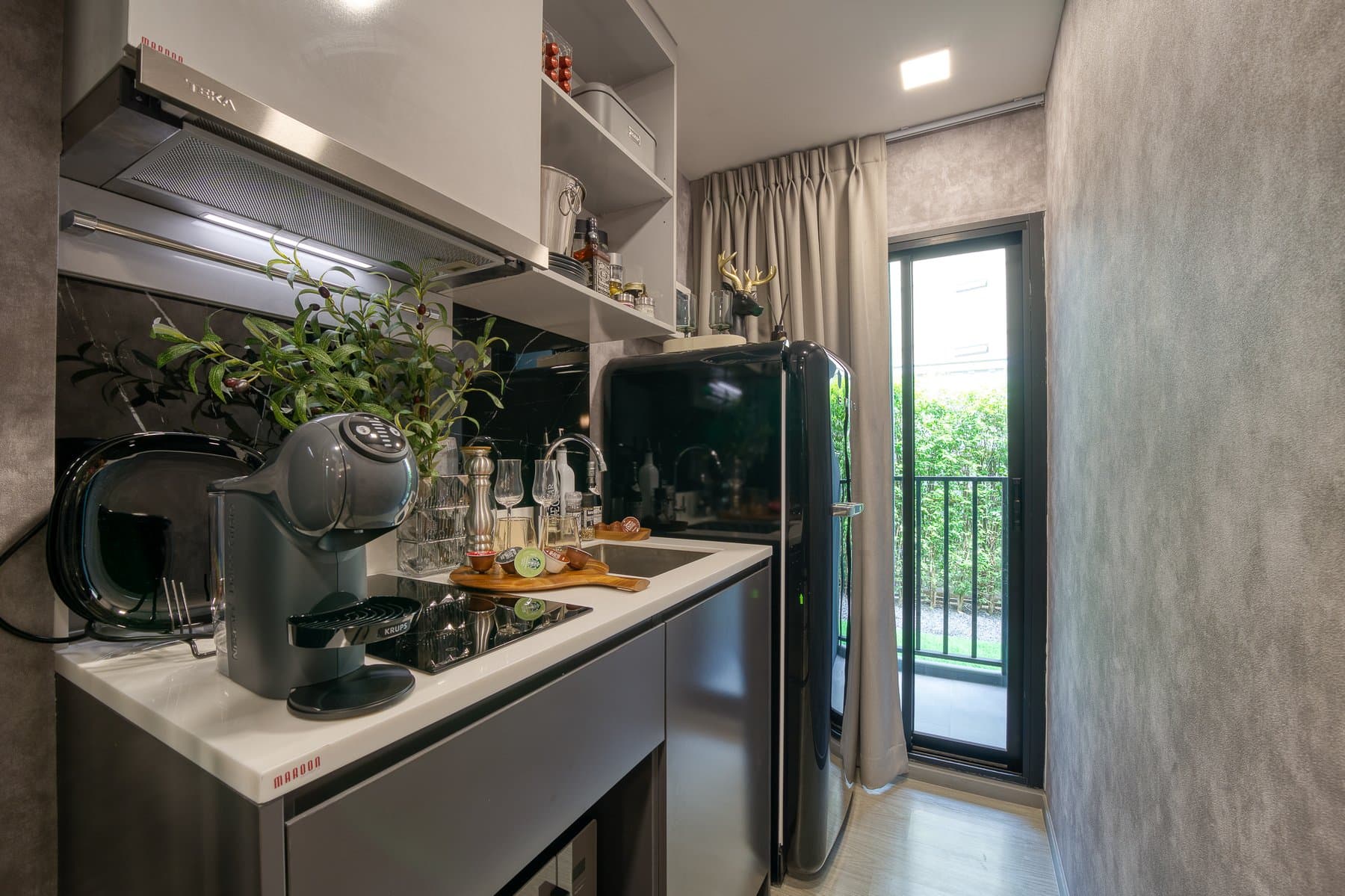 Kitchen counter in a furnished show unit at Maroon Ratchada 32, with a coffee machine, open shelving and a glazed door to the balcony