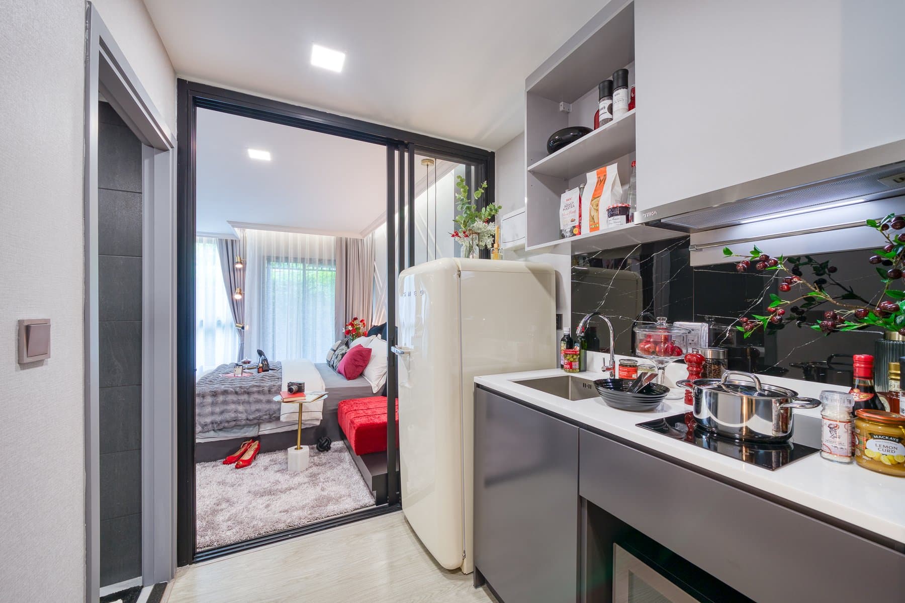 Kitchen of a furnished show unit at Maroon Ratchada 32, with a dark counter, a cream fridge and a mirrored partition through to the bedroom