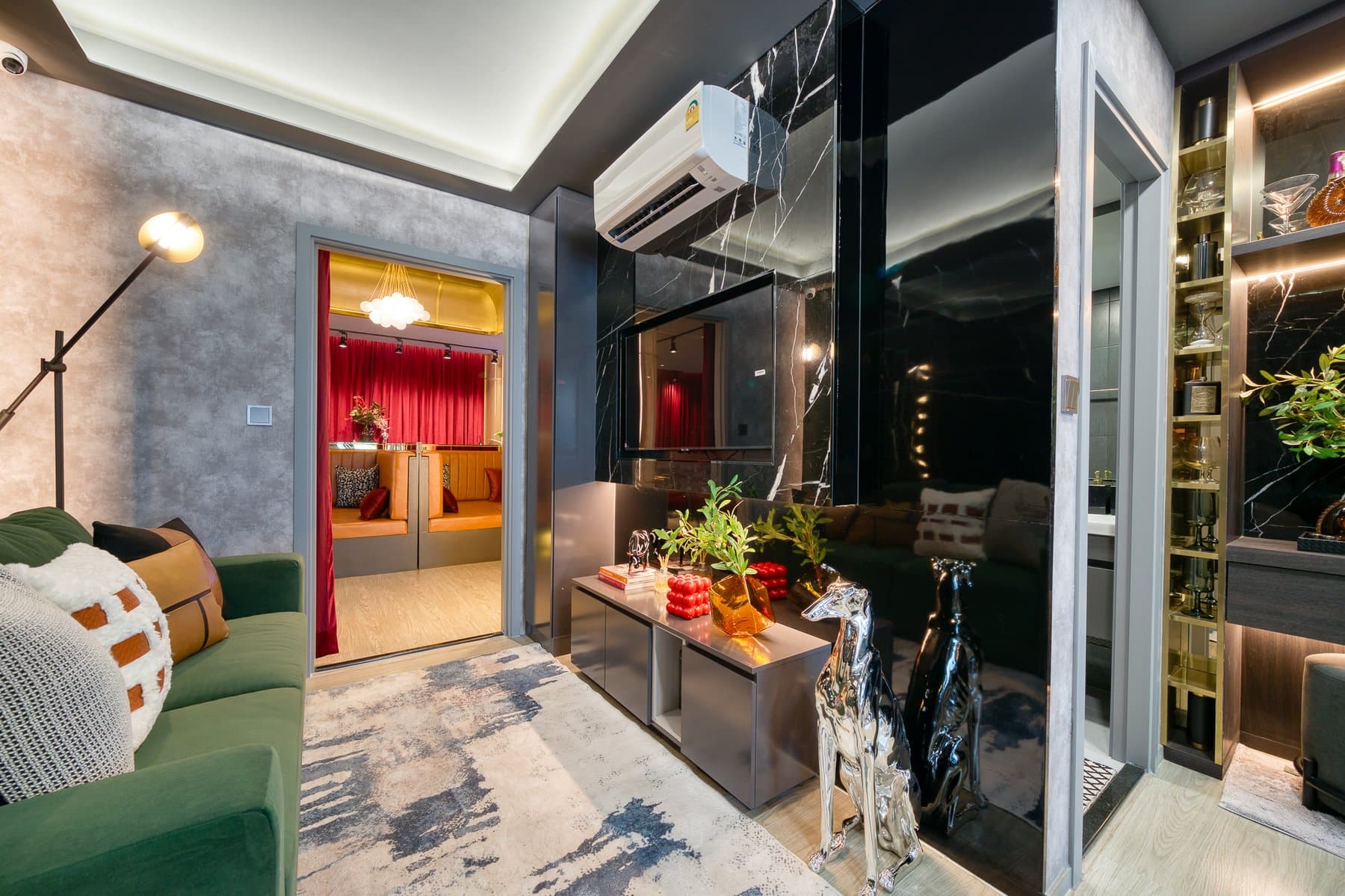 Living area of a furnished show unit at Maroon Ratchada 32, with a green sofa, a patterned rug and a mirrored wardrobe wall
