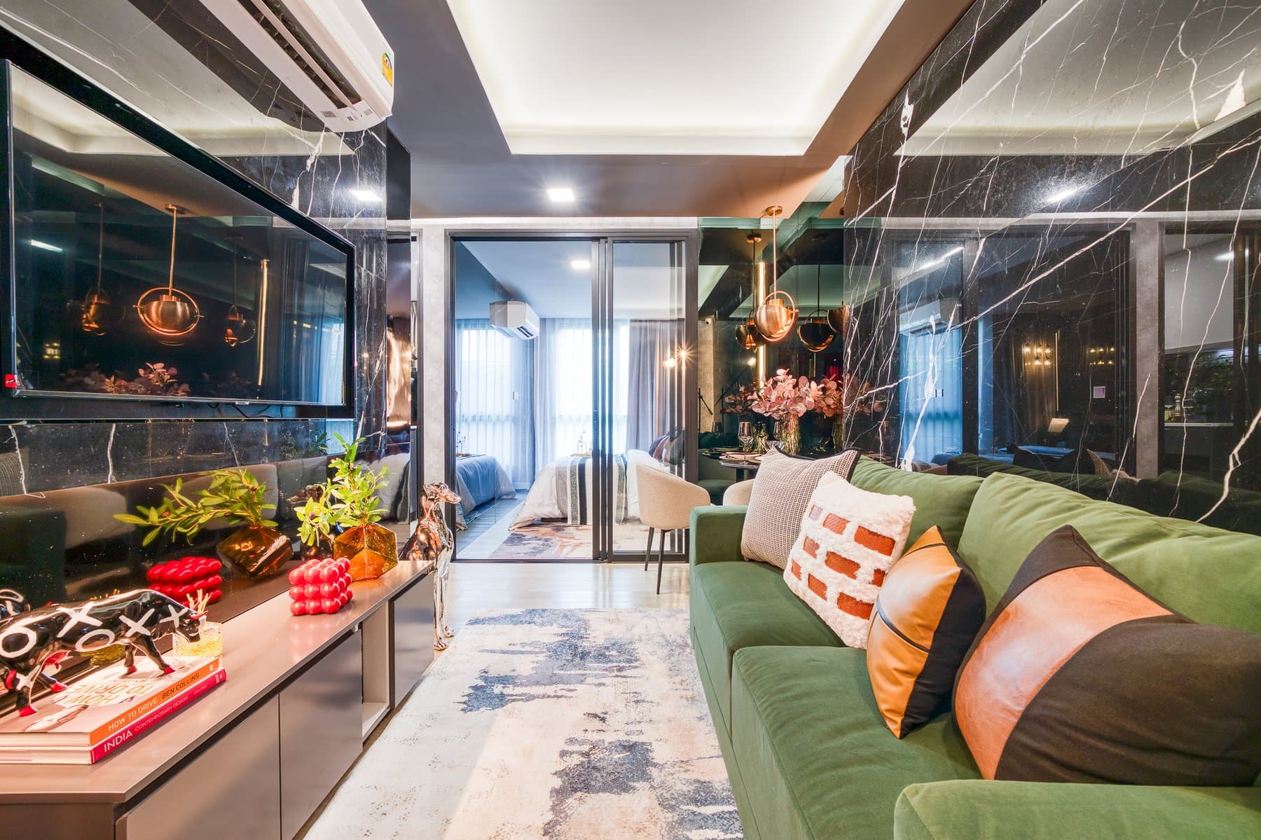 Living area of a furnished show unit at Maroon Ratchada 32, with a green sofa against a dark marble feature wall and a glazed partition beyond