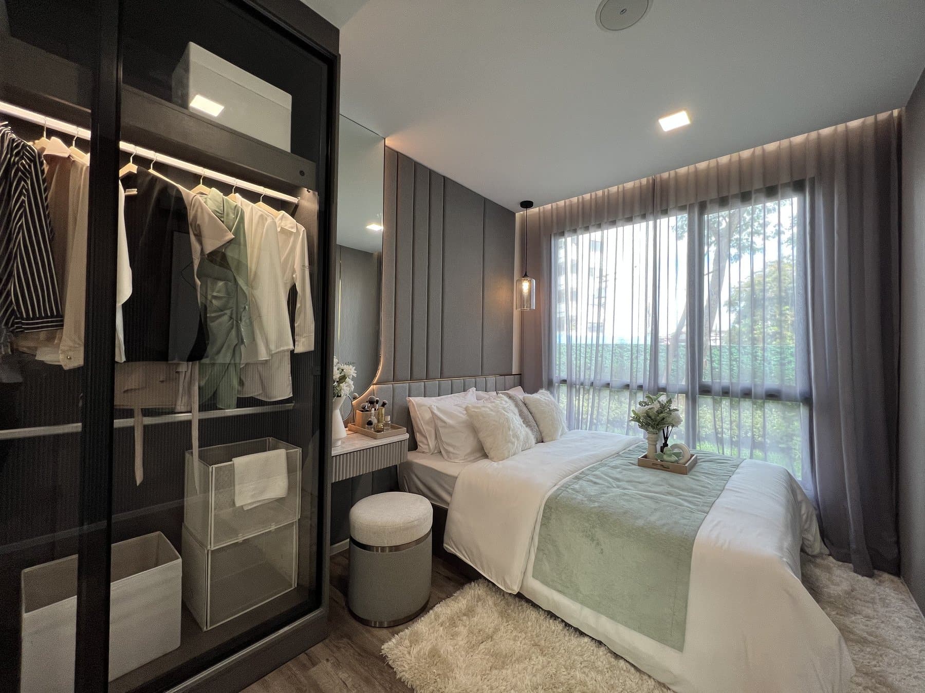 Bedroom of a furnished show unit at Modiz Vault, with a glazed walk-in wardrobe, a padded stool and full-height curtains