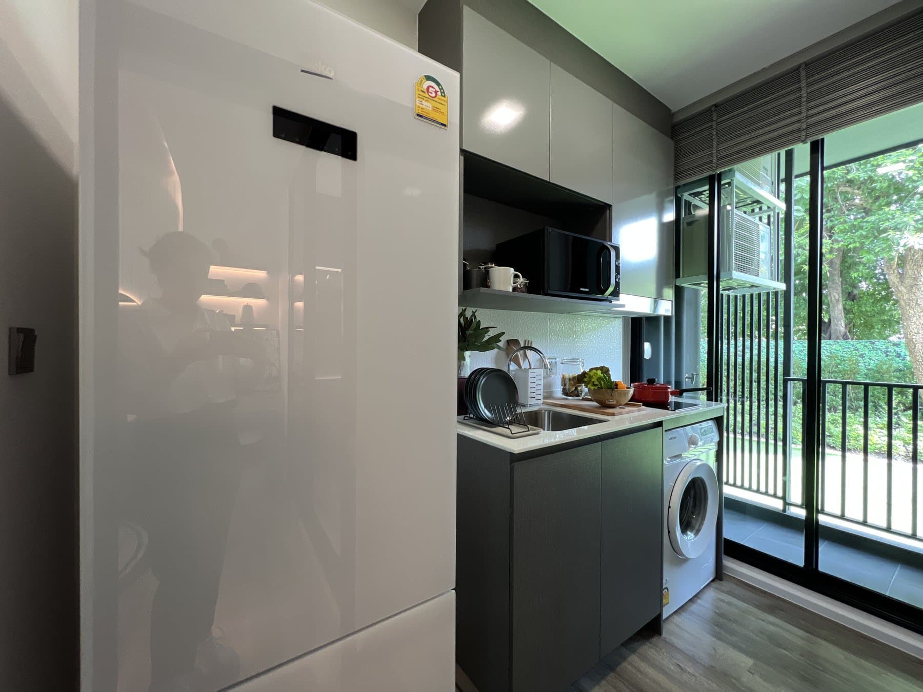 Galley kitchen in a furnished show unit at Modiz Vault, with a microwave, a washing machine and a glazed wall to the balcony