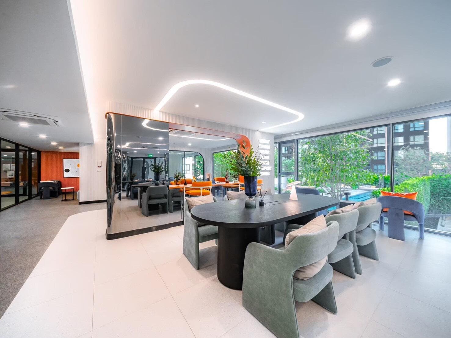 Photograph of the residents' co-working and social lounge with a long oval table, upholstered armchairs and full-height glazing onto the pool courtyard.