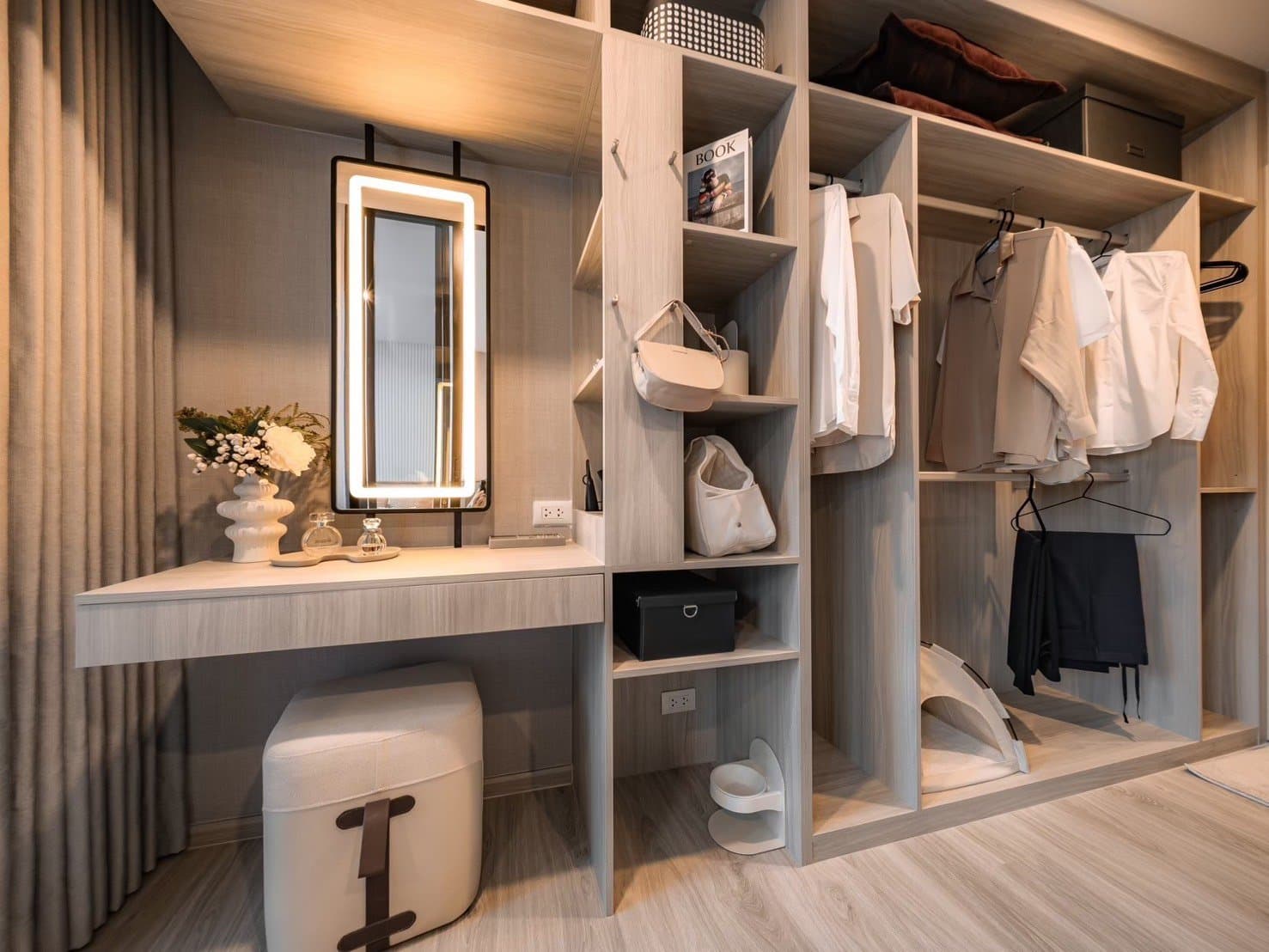 Dressing area of a furnished show unit at Origin Play Sri Udom Station, with an open wardrobe system, a lit vanity mirror and a padded stool
