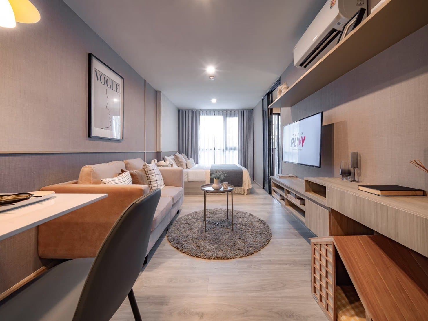 Living area of a furnished show unit at Origin Play Sri Udom Station, with a television wall, a study desk and a round rug between the sofa and the bed