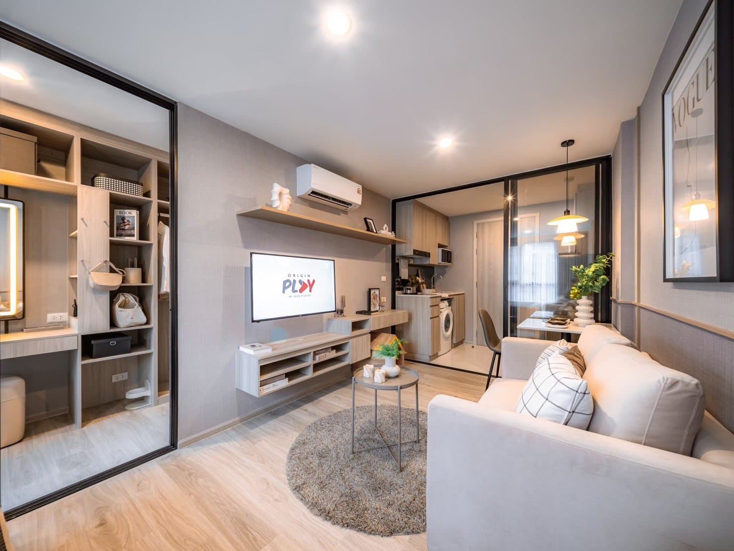 Furnished show unit at Origin Play Sri Udom Station looking across the sofa to the television and the compact kitchen behind a glazed partition