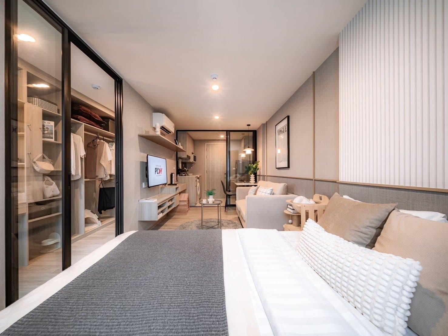 Full length of a furnished show unit at Origin Play Sri Udom Station, from the bed past the mirrored wardrobe to the living area and its window